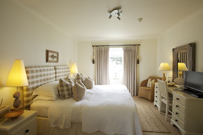 A bedroom at luxury hotel in Cornwall, the Driftwood, with a huge double bed and patio doors leading to a balcony and view of the sea.